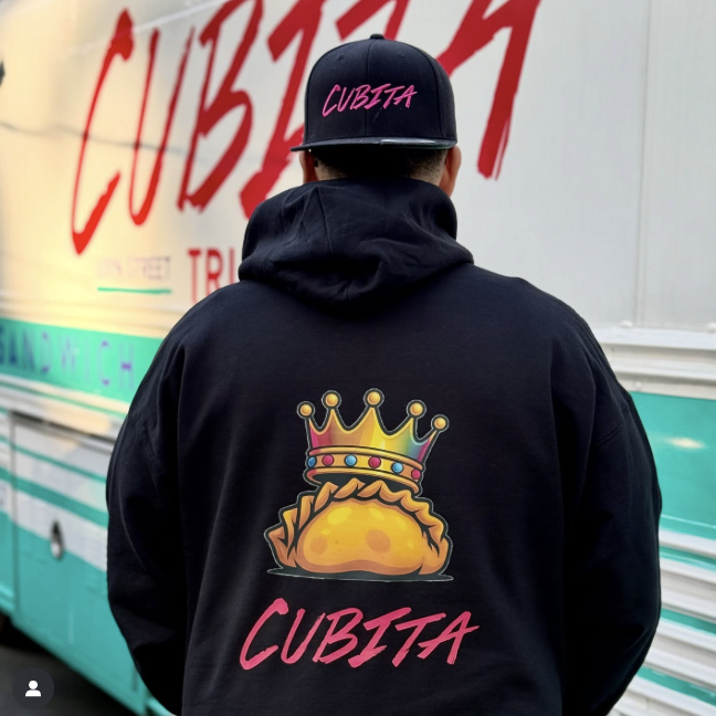 Cubita hoodie with empanada crown artwork in front of the truck